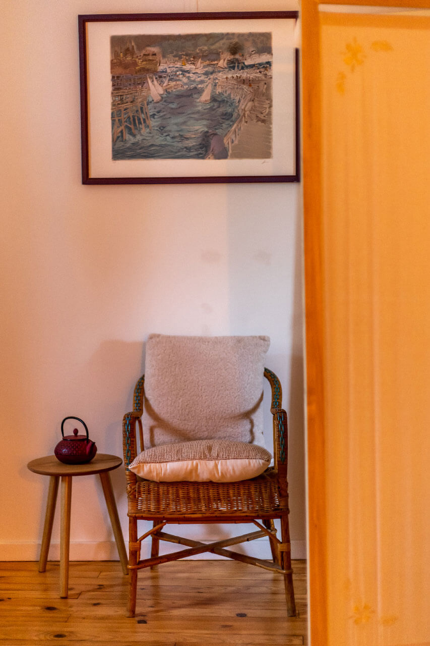 Photo d'une chaise en rotin présente dans le cabinet, avec à côté une petite table et une theillère posée dessus.